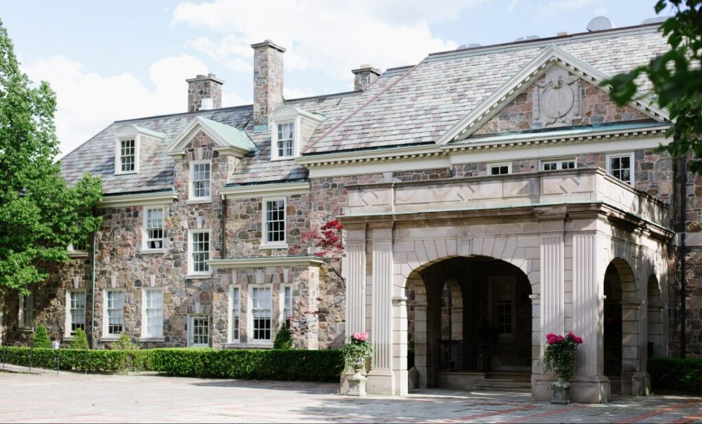 Exterior view of Graydon Hall Manor in Toronto, a stately stone estate with an arched porte-cochère entrance, dormer windows, and manicured hedges.