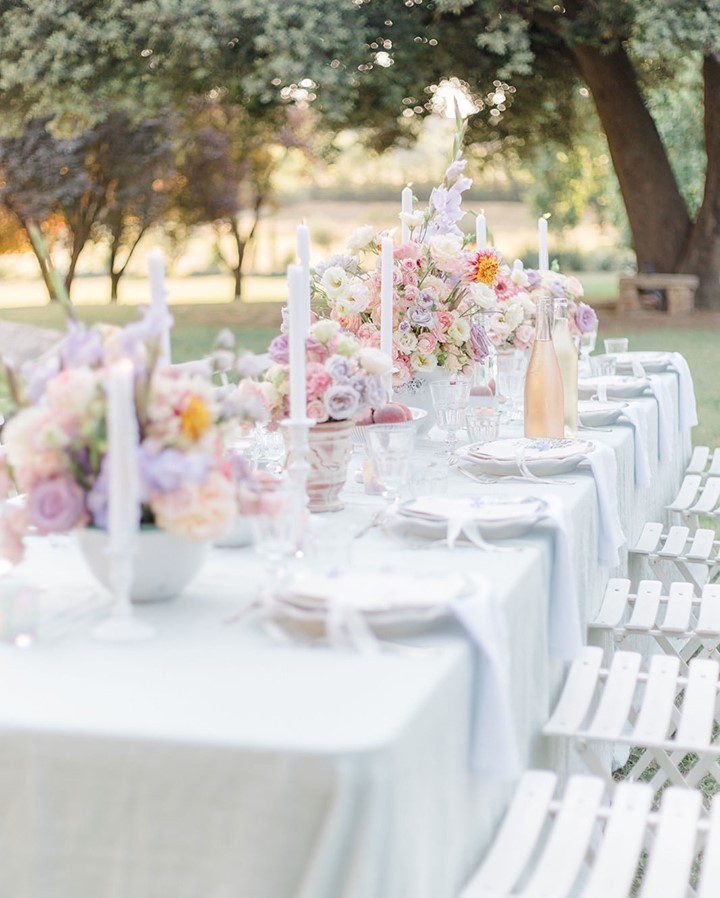Elegant outdoor table setting with white chairs, pastel floral arrangements, and tall candles, creating a serene and sophisticated atmosphere, planned by Ajna of Oui Mon Coeur.