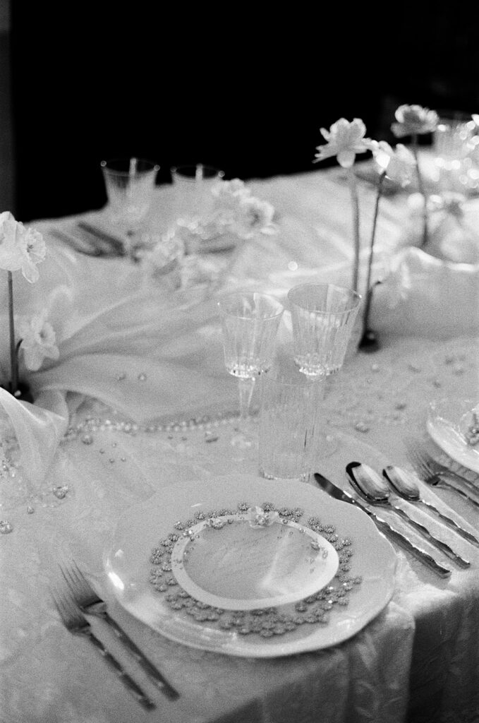 Elegant black and white table setting with ornate plates, crystal glasses, and delicate flowers on a flowy tablecloth. A serene, sophisticated ambiance.