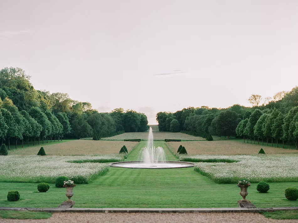 Formal gardens and fountain at Château de Champlâtreux, framed by manicured lawns and tree-lined avenues.